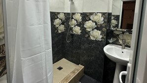 Casa de banho com chuveiro, lavatório e espelho.