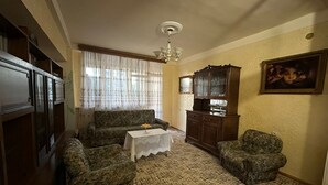 Sala de estar com sofá, duas poltronas, uma mesinha com vaso, aparador com copos e lustre.