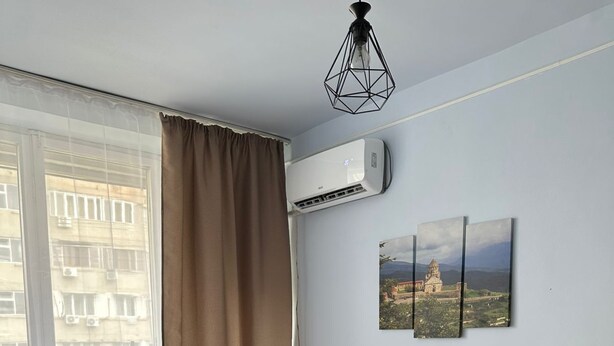Quarto de hotel com duas camas, uma janela com cortinas, aparelho de ar condicionado e um quadro pendurado na parede.