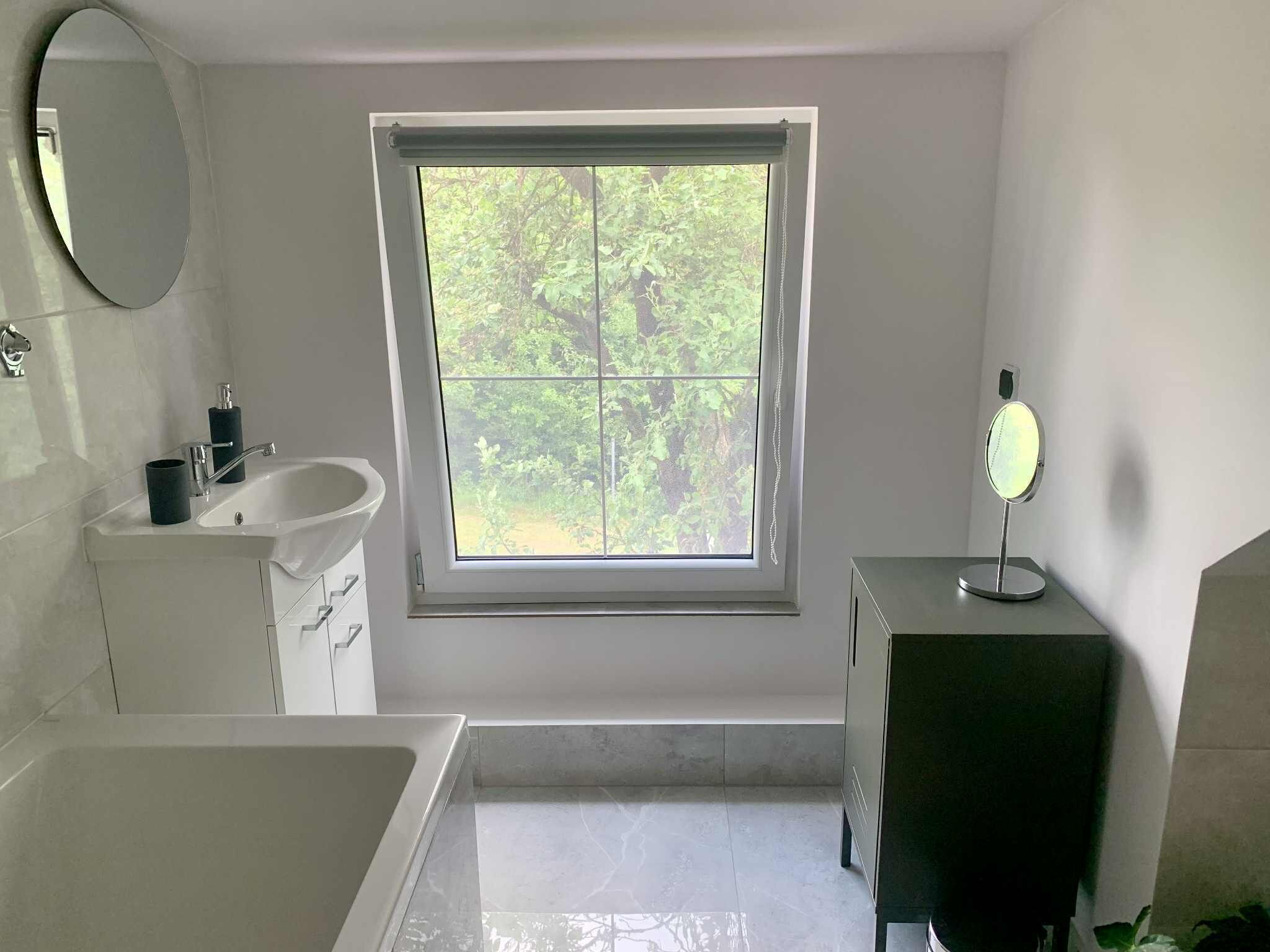Une salle de bain moderne avec une baignoire, un lavabo, un miroir et une fenêtre.