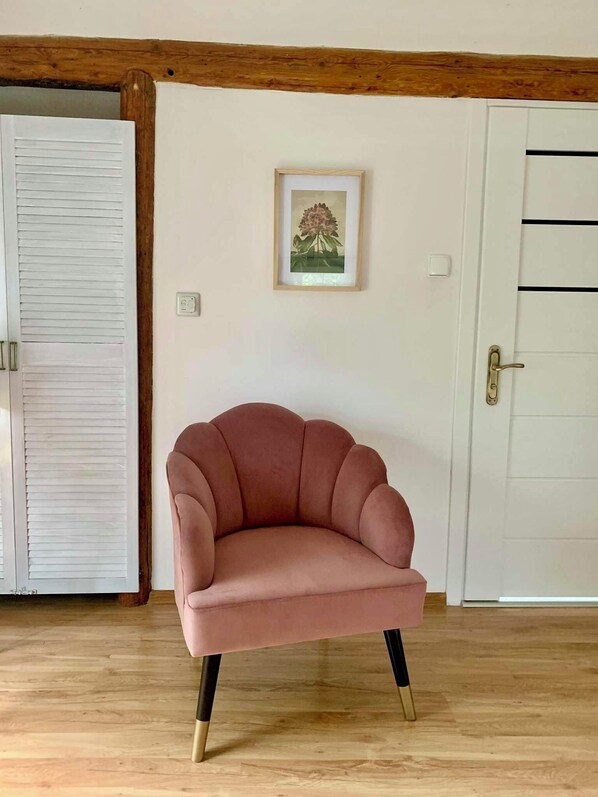 A pink armchair with wooden legs in a room with wooden flooring, a white door, and a framed picture on the wall.