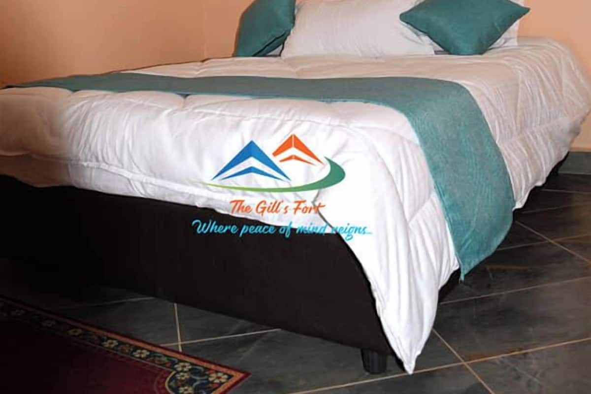 Un lit bien fait, recouvert d’une couverture blanche et turquoise, avec un tableau encadré représentant une voiture accroché au mur, et un logo imprimé sur la couverture.