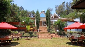 Une maison avec un jardin devant, un escalier menant à l’entrée et un espace extérieur aménagé avec des parasols rouges.