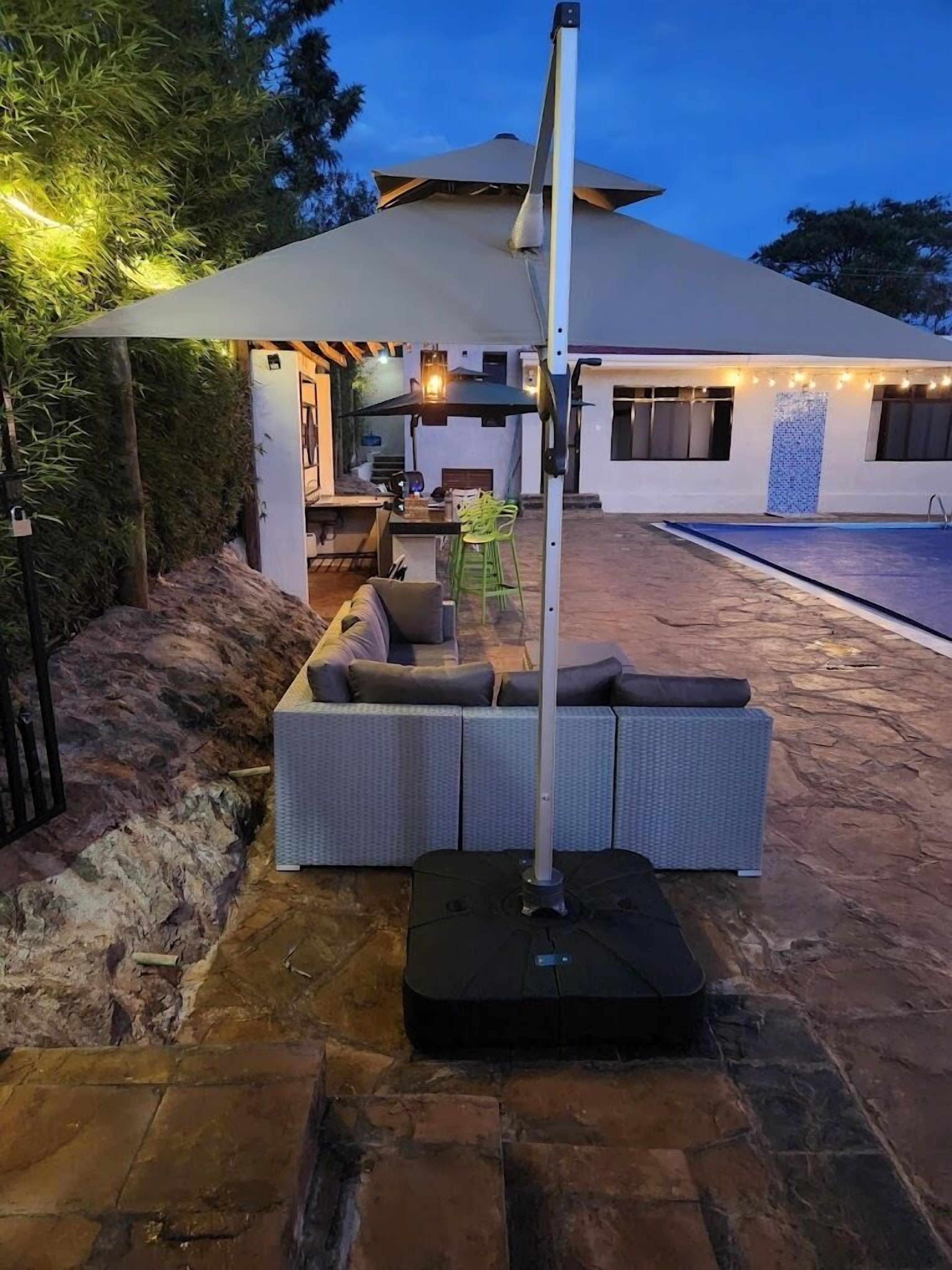An outdoor seating area with a large umbrella, a stone patio, and a pool in the background.