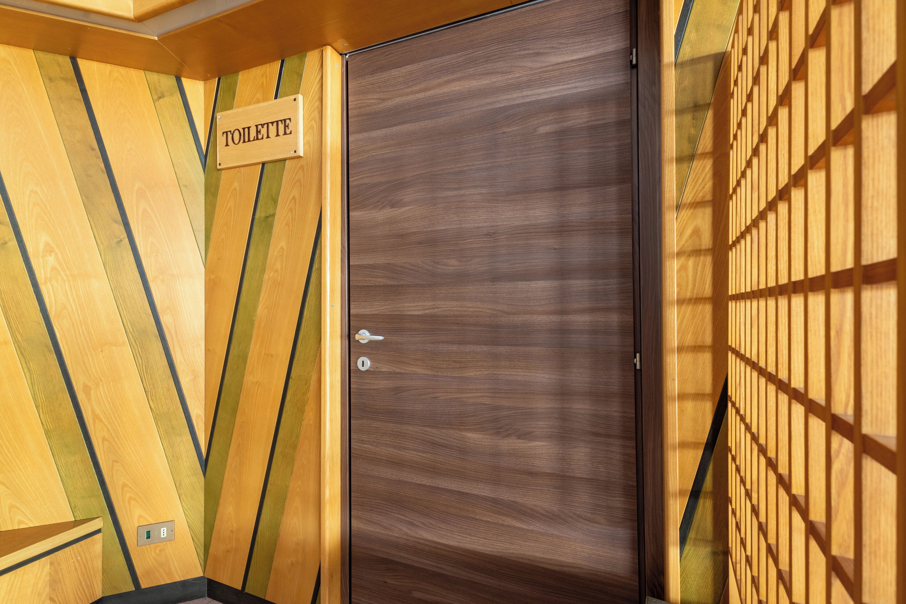Un mur en bois avec une pancarte indiquant « TOILETTES » et une porte dotée d’un trou de serrure.