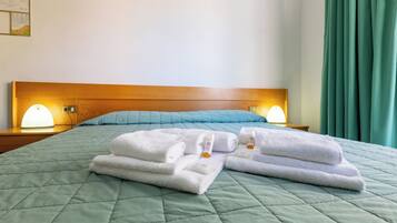 Een opgemaakt bed met een groene gewatteerde spreideken, twee witte handdoeken en twee bedlampjes op een houten hoofdbord.