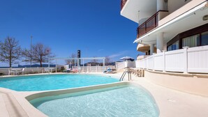 Ein Swimmingpool mit klarem, blauem Wasser, einem weißen Zaun und einem Gebäude mit Balkon.