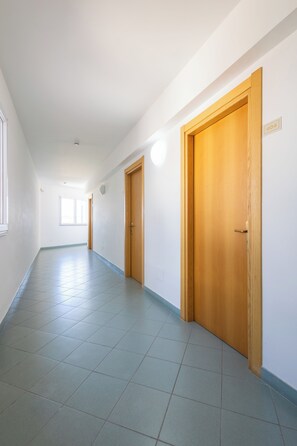 A corridor with tiled flooring, wooden doors, and a window at the end. - Hotiday Alghero Spiaggia (Alghero)