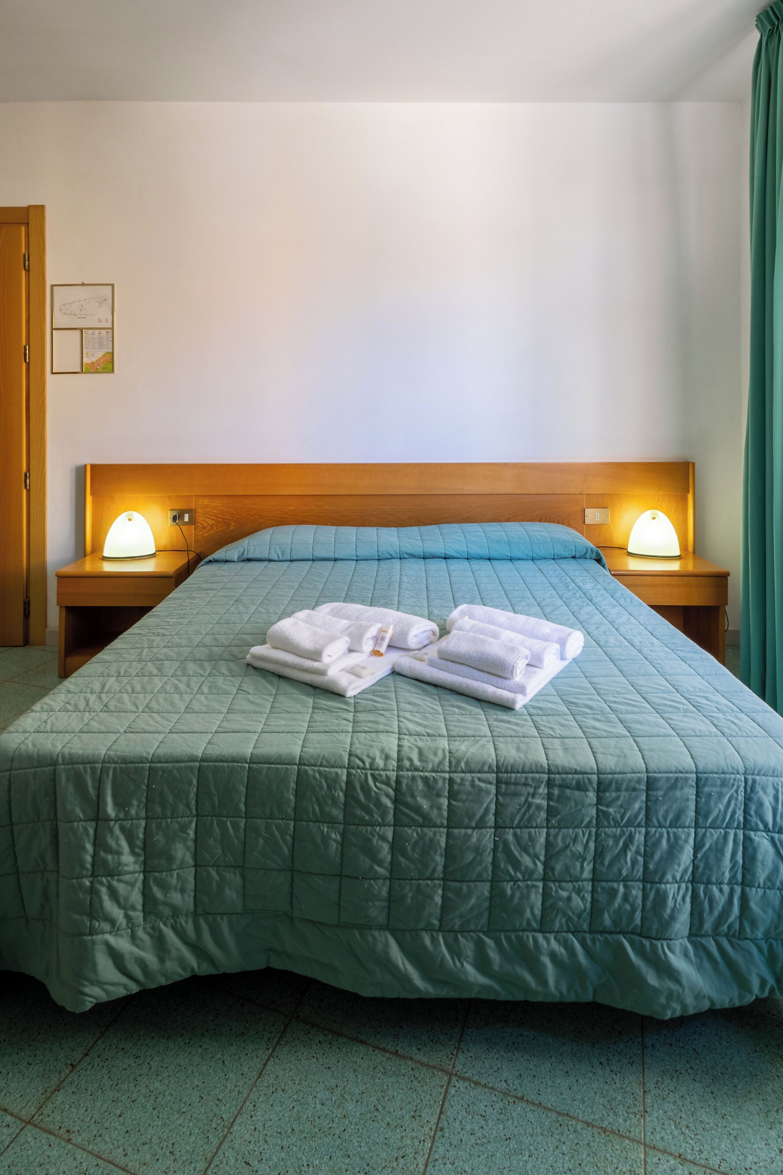 Una habitación de hotel con una cama, dos lámparas de noche, una mesita de noche y un reloj en la pared.