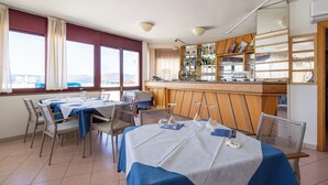 Ein Essbereich mit Tischen für vier Personen, eine Bar mit einer Auswahl an Flaschen und Blick durch große Fenster.