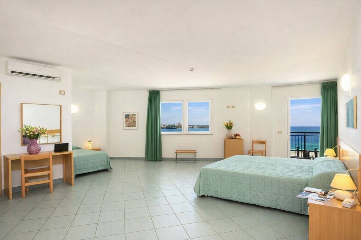 Une chambre d’hôtel avec un lit, un bureau, une chaise et une vue sur la mer.