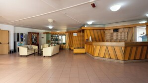 Ein Empfangsbereich mit einem Holzbüro, einer Couch, einem Bücherregal und einem Automaten.