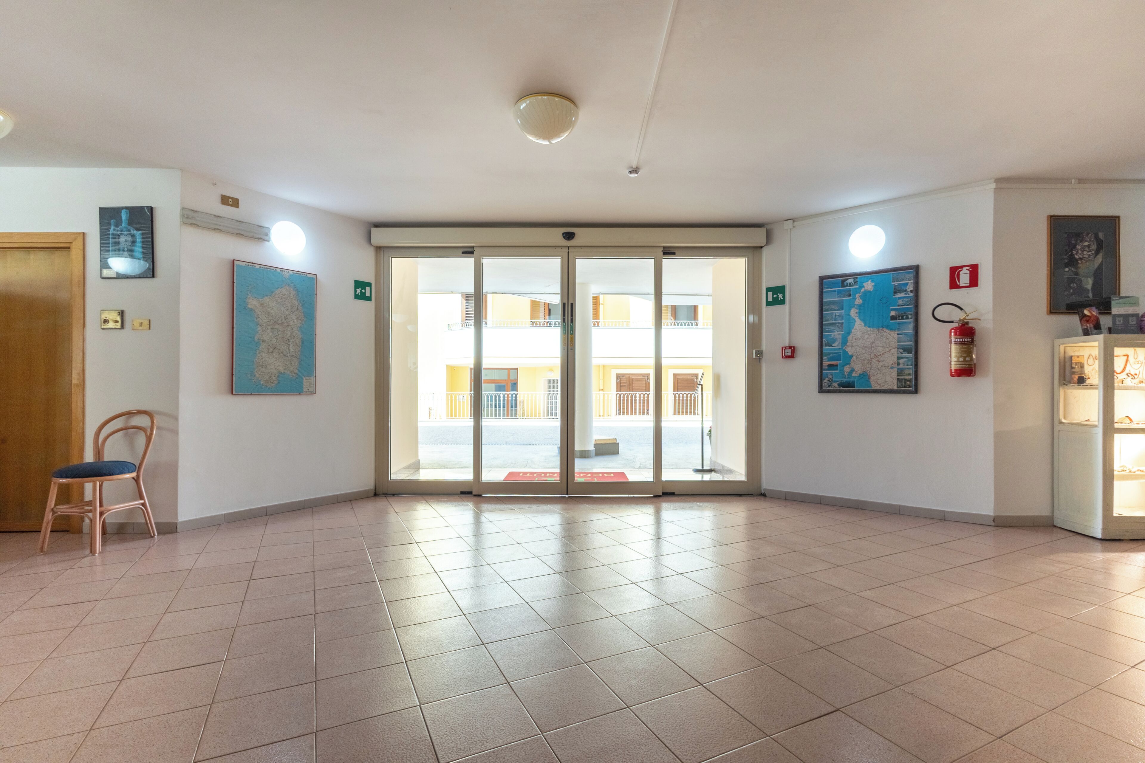 A hotel lobby with a tiled floor, a wooden chair, a fire extinguisher, and a map on the wall.