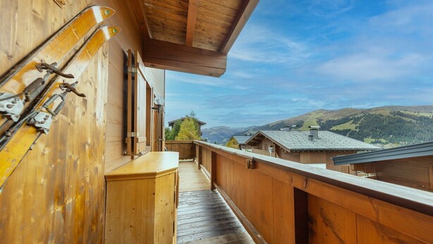 Un balcon en bois avec du matériel de ski, une armoire en bois et une vue sur des bâtiments et des collines.