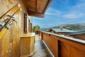 A wooden balcony with ski equipment, a wooden cabinet, and a view of buildings and hills. - Steinadler Silberleiten Apartment with Mountain View, Terrace and Wi-Fi (Hochkrimml)