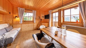 L’intérieur d’un chalet en bois, avec un canapé, une table à manger et des fenêtres donnant sur un paysage agréable.