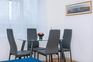 A dining area with a glass table and four grey chairs. A bowl of fruit is on the table. - Spacious 3BR S/E London Flat in Penge with Parking sleeps 6 (London)
