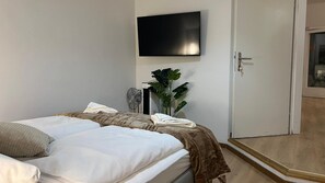 Ein Hotelzimmer mit Bett, Wandfernseher, Pflanze und einer Tür zu einem Balkon.