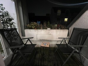 Ein Balkon mit zwei Stühlen und einem kleinen Tisch, mit Blick auf einen Garten und ein Gebäude.