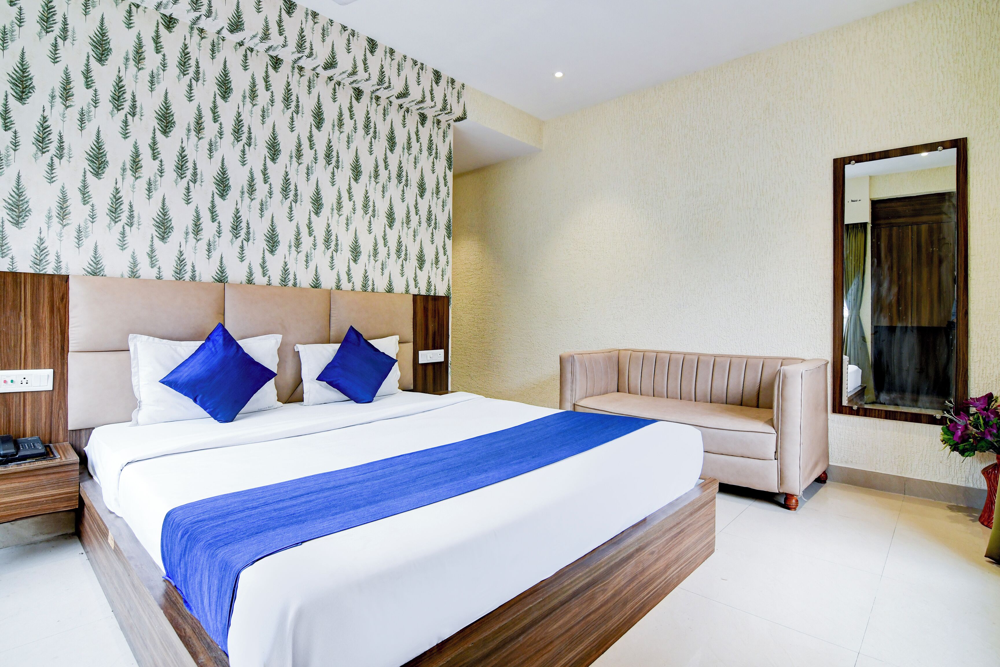 Ein Hotelzimmer mit einem großen Bett, einer Couch, einem Spiegel und einer Wand mit einem Blattmuster.