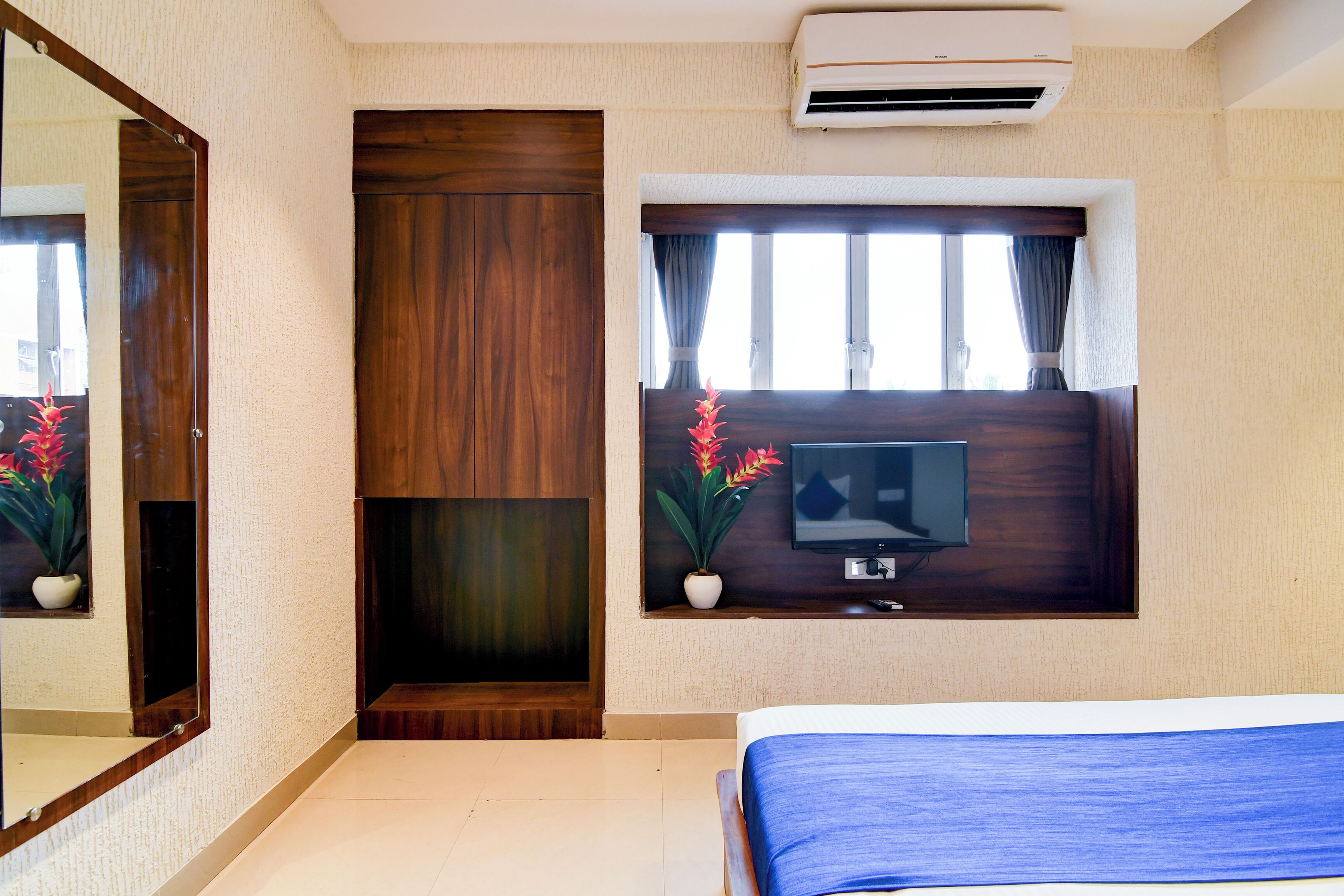 Une chambre d’hôtel avec un lit, un téléviseur fixé au mur, une porte en bois et une fenêtre avec des rideaux.