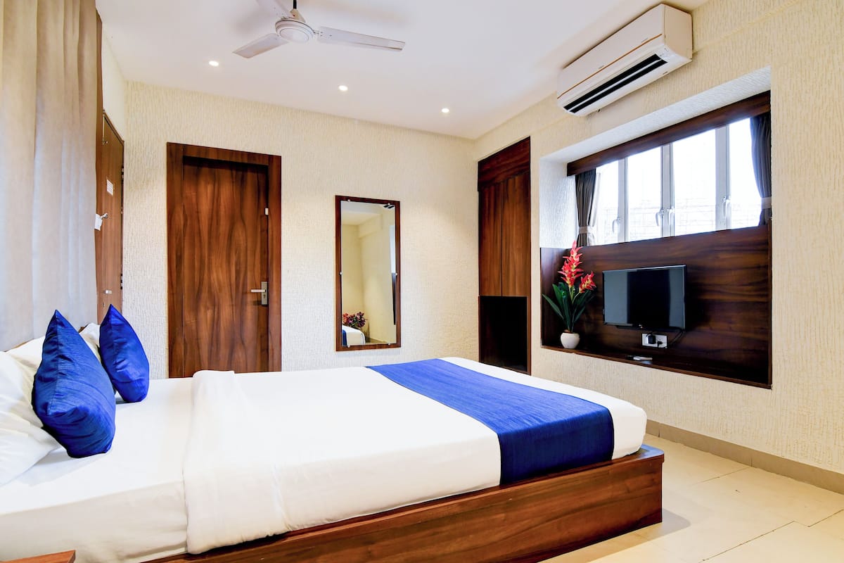Una habitación de hotel con cama, televisión, aire acondicionado y ventana con cortinas.