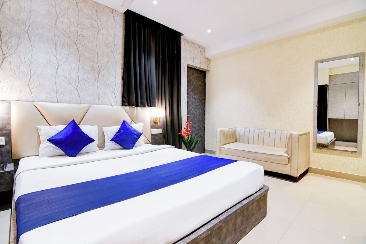 Una habitación de hotel moderna con una cama grande, un sofá, un espejo y una mesita de noche.