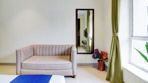 A room with a beige sofa, a mirror, a window with curtains, and a vase with flowers. - Lake View - by Brill Rooms (Kolkata)