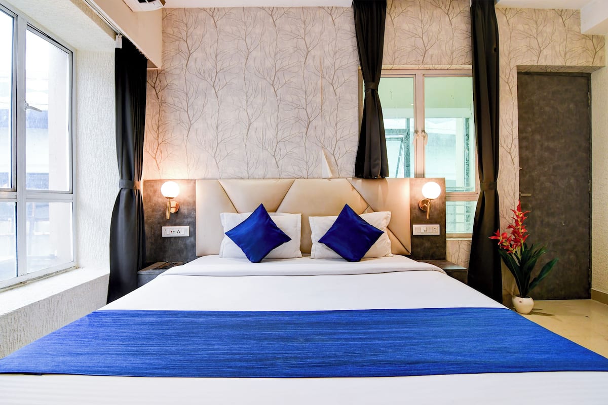 Habitación de hotel con una cama grande, dos lámparas de noche, una ventana con cortinas, una puerta y una planta en maceta.