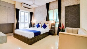 A modern hotel room with a large bed, a ceiling fan, a window with curtains, a door, and a small seating area. - Lake View - by Brill Rooms (Kolkata)