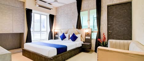 Una habitación de hotel moderna con una cama grande, un ventilador de techo, una ventana con cortinas, una puerta y una pequeña zona de estar.