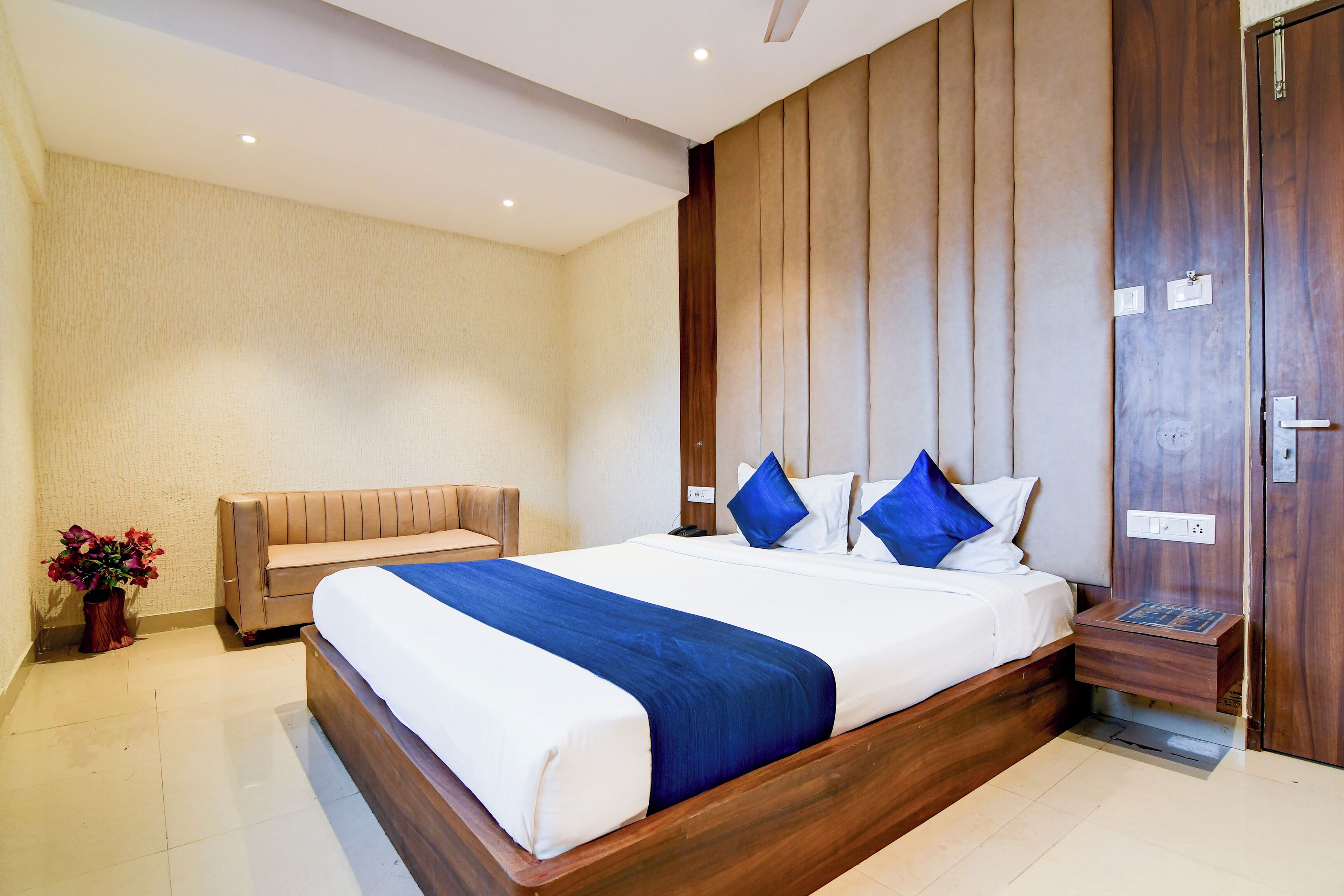 Une chambre d’hôtel moderne avec un grand lit, une tête de lit en bois, une table de chevet et un banc.