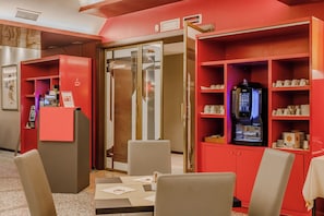 A hotel lobby with red decor, a coffee machine, and seating area. - Hotiday Venezia Marco Polo (Mestre)