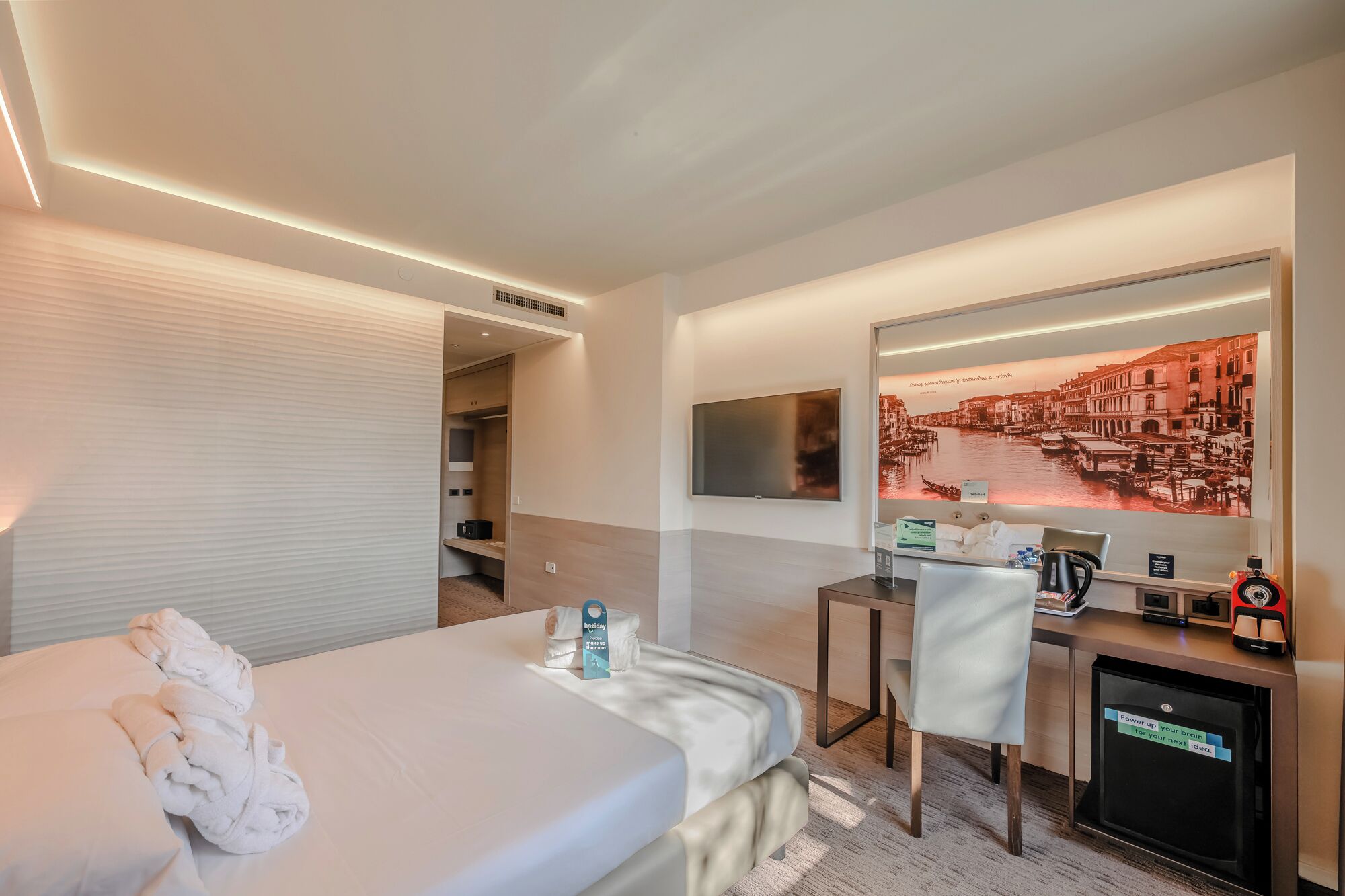 Una habitación de hotel con una cama, un escritorio, un televisor y un espejo.