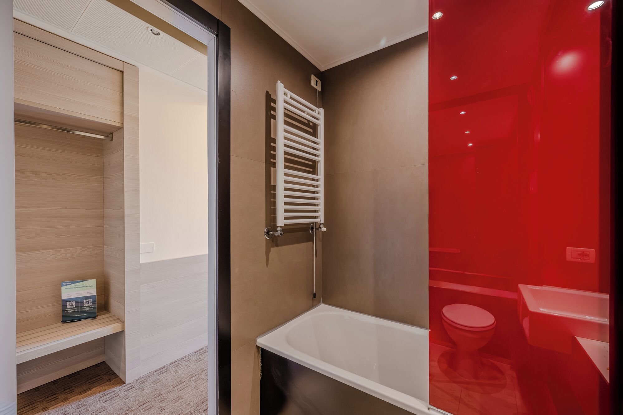 A bathroom with a white bathtub, a red shower enclosure, and a wooden vanity with a towel rack.