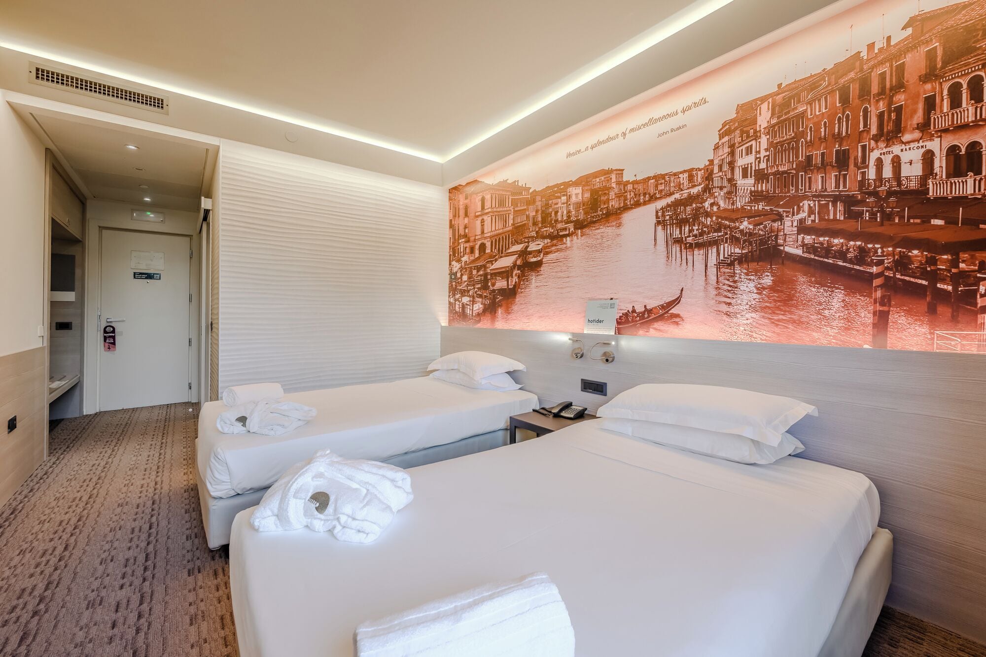 Een hotelkamer met twee bedden, een groot muurdecor met Venetië en een minibar.