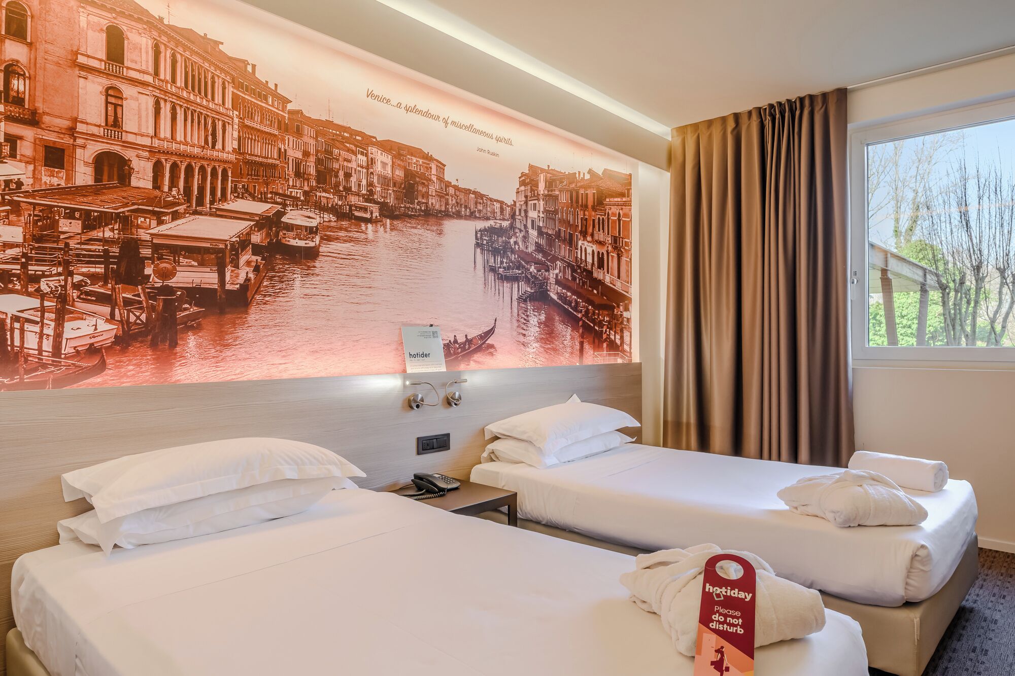A hotel room with two beds, a large wall mural of Venice, a window with curtains, and a 'holiday please do not disturb' tag.