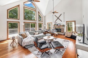 Un salón espacioso con techo alto, ventanas grandes, chimenea y televisor.