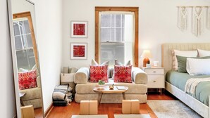Un dormitorio moderno con un sofá, una mesita de noche con lámpara, una cama con ropa de cama verde, un espejo grande y dos esterillas de yoga.