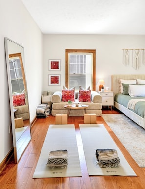 Un dormitorio moderno con un sofá, una mesita de noche con lámpara, una cama con ropa de cama verde, un espejo grande y dos esterillas de yoga.