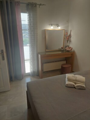 Une chambre à coucher comprenant un lit, une coiffeuse avec un miroir, un radiateur et une fenêtre avec des rideaux.