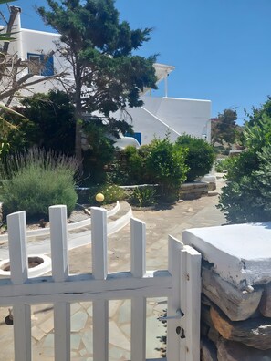 Un bâtiment blanc avec une porte bleue, entouré de verdure et bordé d’un chemin de pierres.