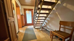 A hallway with a wooden chair, a mat, and a staircase. - Old farm f. Teams and families in the wine village with excellent connections (Albig)