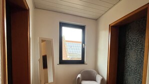 A room with a wooden parquet floor, a small window with a view of a building, a white easel, and a grey armchair. - Old farm f. Teams and families in the wine village with excellent connections (Albig)
