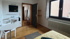 A bedroom with a bed, a desk with a chair, a window, and a bathroom visible through an open door. - Old farm f. Teams and families in the wine village with excellent connections (Albig)
