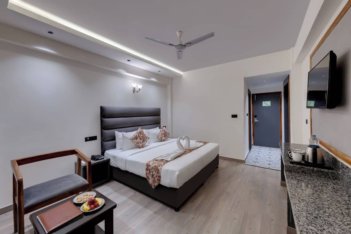 A modern hotel room with a bed, a desk with a chair, a flat-screen TV, and a ceiling fan.