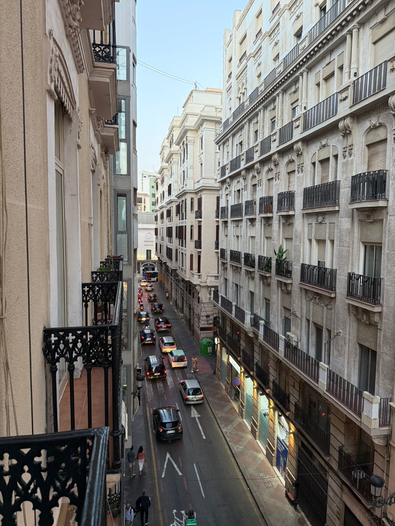 A street view of a city with tall buildings, a narrow road, and cars.