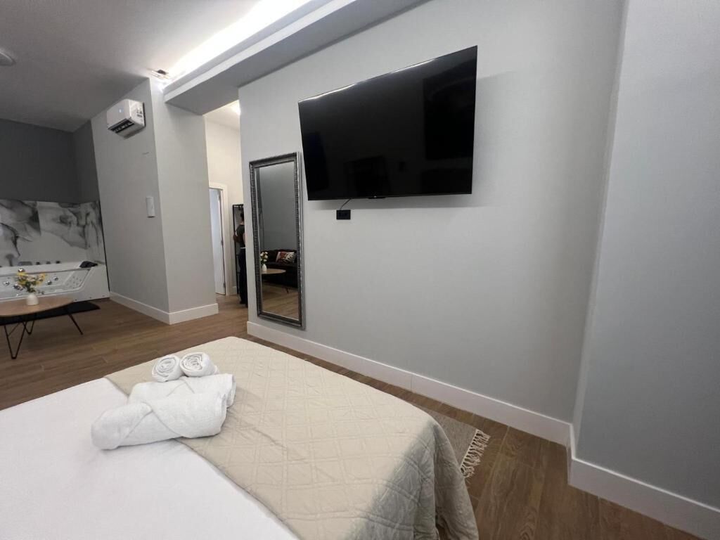 Una habitación de hotel moderna con una cama grande, un televisor de pantalla plana montado en la pared, un área de spa con una mesa de masaje y una pequeña mesa con toallas.