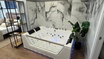 Un baño moderno con una bañera independiente, pared de mármol y un estante pequeño con artículos de aseo.