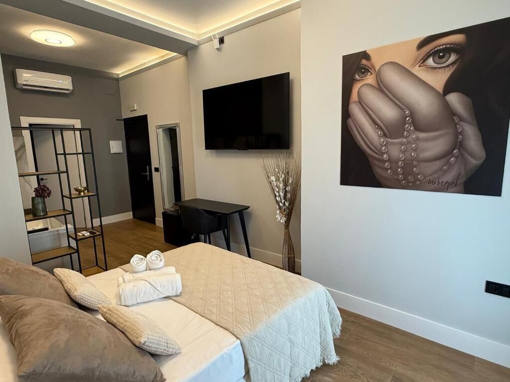 A modern bedroom with a bed, pillows, a TV, and a painting on the wall.